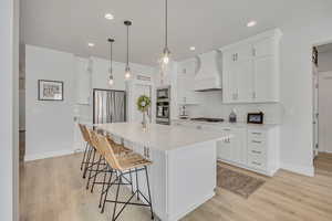 Kitchen featuring custom range hood, appliances with stainless steel finishes, a breakfast bar, backsplash, and light wood-style flooring