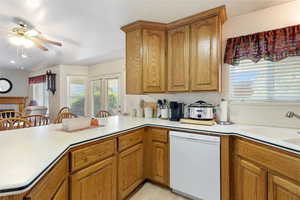 Kitchen with white dishwasher, ceiling fan, light countertops, brown cabinets, and a sink