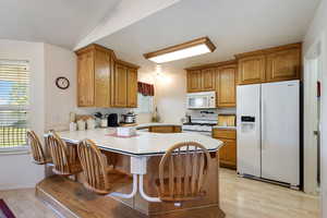 Kitchen with white appliances, light wood-style flooring, a peninsula, light countertops, and brown cabinets