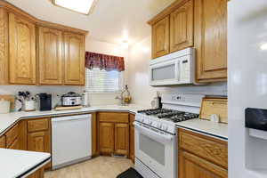 Kitchen with white appliances, a sink, brown cabinets, light countertops, and light wood finished floors