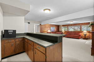 Kitchen featuring a textured ceiling, wood walls, dark countertops, a peninsula, and brown cabinets
