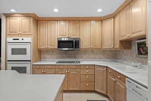 Kitchen with white appliances, a sink, light countertops, recessed lighting, and backsplash