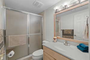 Bathroom with vanity, toilet, a shower stall, and a textured ceiling