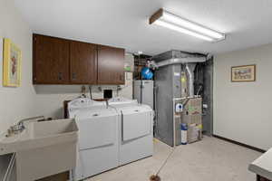 Laundry area with washer and dryer, cabinet space, light floors, a textured ceiling, and heating unit