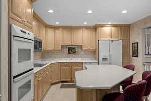 Kitchen featuring white appliances, a kitchen breakfast bar, light countertops, recessed lighting, and light brown cabinets
