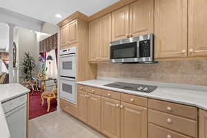 Kitchen with white appliances, light countertops, light tile patterned flooring, light brown cabinetry, and recessed lighting