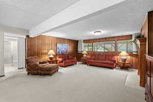 Living room featuring wood walls, a textured ceiling, light carpet, and beam ceiling