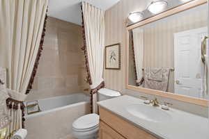 Bathroom featuring wallpapered walls, tiled shower / bath combo, toilet, and vanity