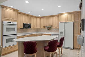 Kitchen with white appliances, light countertops, a sink, a breakfast bar area, and a kitchen island