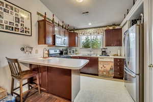Kitchen featuring appliances with stainless steel finishes, a peninsula, a sink, light countertops, and a kitchen breakfast bar