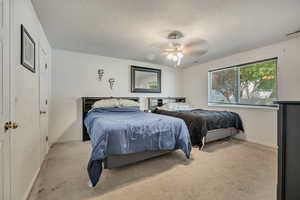 Bedroom with light carpet, baseboards, a textured ceiling, and a ceiling fan