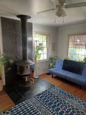 Living room featuring a wood stove, ceiling fan, wood finished floors, and baseboards