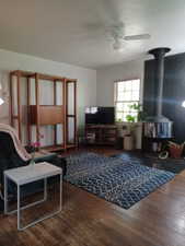 Living room featuring a wood stove, a ceiling fan, and wood finished floors