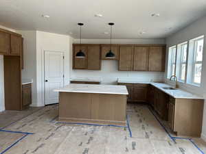 Kitchen featuring a sink, a kitchen island, a textured ceiling, pendant lighting, and brown cabinetry
