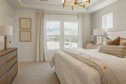 Bedroom featuring multiple windows, a tray ceiling, a chandelier, and light colored carpet