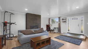 Living room featuring crown molding, baseboards, light wood finished floors, a brick fireplace, and recessed lighting