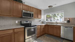 Kitchen with stainless steel appliances, a sink, decorative backsplash, light countertops, and brown cabinetry