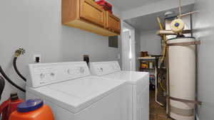Washroom featuring separate washer and dryer, cabinet space, gas water heater, electric panel, and dark stone finish floors