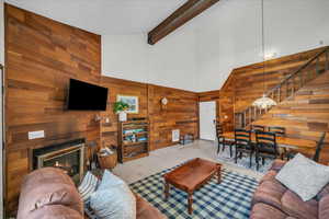 Living area with wooden walls, stairway, high vaulted ceiling, a glass covered fireplace, and beam ceiling