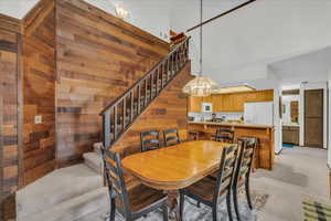 Dining space featuring wood walls, stairs, light carpet, a chandelier, and a towering ceiling
