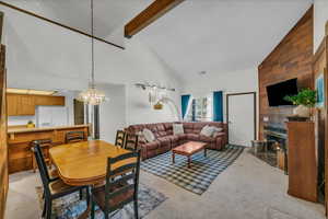Living room with a chandelier, high vaulted ceiling, beam ceiling, a fireplace, and light colored carpet