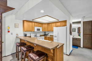 Kitchen featuring white appliances, a peninsula, a breakfast bar area, a textured ceiling, and a sink