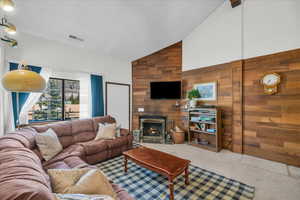 Living area featuring high vaulted ceiling, wood walls, carpet, and a fireplace