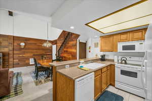 Kitchen with white appliances, a sink, wooden walls, a peninsula, and brown cabinets