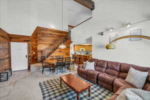 Living room with a towering ceiling, stairs, wooden walls, light tile patterned flooring, and light colored carpet
