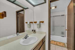 Bathroom with vanity, toilet, tile patterned floors, and combined bath / shower with glass door