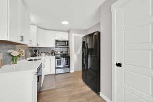 Kitchen featuring stainless steel appliances, a sink, light countertops, tasteful backsplash, and light wood finished floors