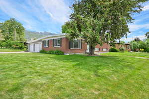 View of front of property featuring brick siding, a garage, asphalt driveway, a front yard, and a mountain view