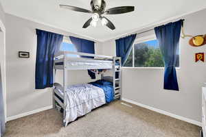 Carpeted bedroom with baseboards, multiple windows, and a ceiling fan