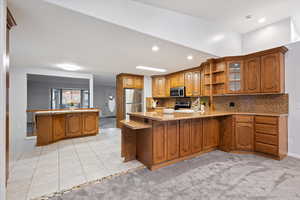 Kitchen with stainless steel appliances, a peninsula, brown cabinetry, a sink, and light stone counters