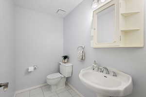 Bathroom featuring a sink, toilet, baseboards, and tile patterned flooring