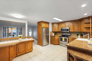 Kitchen featuring stainless steel appliances, open shelves, a sink, brown cabinets, and backsplash