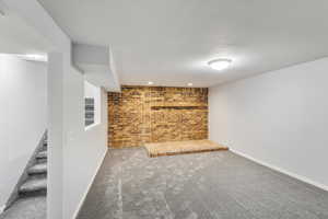 Finished basement with brick wall, carpet flooring, stairway, baseboards, and recessed lighting