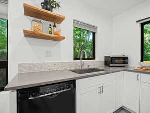 Kitchen with black dishwasher, a sink, stainless steel microwave, decorative backsplash, and white cabinetry