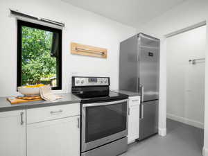 Kitchen featuring stainless steel appliances, white cabinets, finished concrete flooring, dark countertops, and baseboards