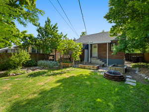 Back of house featuring brick siding, an outdoor fire pit, and a shingled roof