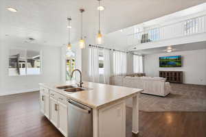 Kitchen featuring stainless steel dishwasher, a sink, baseboards, dark wood-style floors, and an island with sink