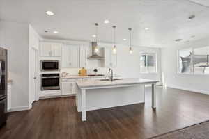 Kitchen featuring appliances with stainless steel finishes, wall chimney exhaust hood, a sink, baseboards, and dark wood-type flooring