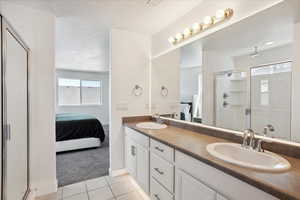 Ensuite bathroom featuring a shower stall, tile patterned flooring, double vanity, and baseboards