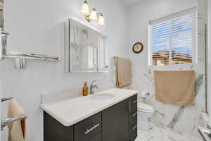 Full bath with vanity, marble finish flooring, toilet, a marble finish shower, and wainscoting