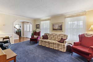 Living room with crown molding, carpet floors, a textured ceiling, stairs, and arched walkways