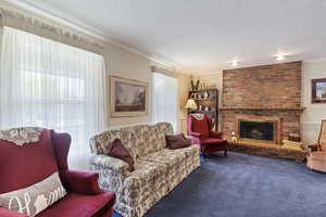 Living area featuring a textured ceiling, crown molding, carpet flooring, and a brick fireplace