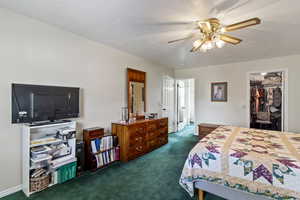 Bedroom with dark colored carpet, ceiling fan, a walk in closet, a textured ceiling, and a bathroom