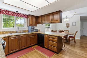 Kitchen with dishwasher, a sink, light countertops, a peninsula, and light wood finished floors
