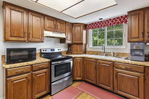 Kitchen featuring  range with electric stovetop, under cabinet range hood, a sink, brown cabinets, and light countertops