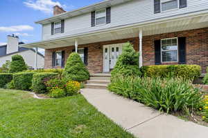 View of front of home with covered porch, brick siding, a chimney, and a front yard